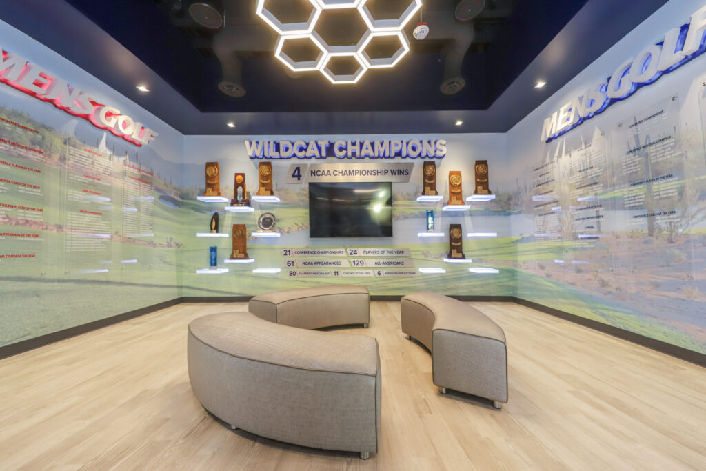 Interior of an open room with golf awards on the wall and rounded benches in the center