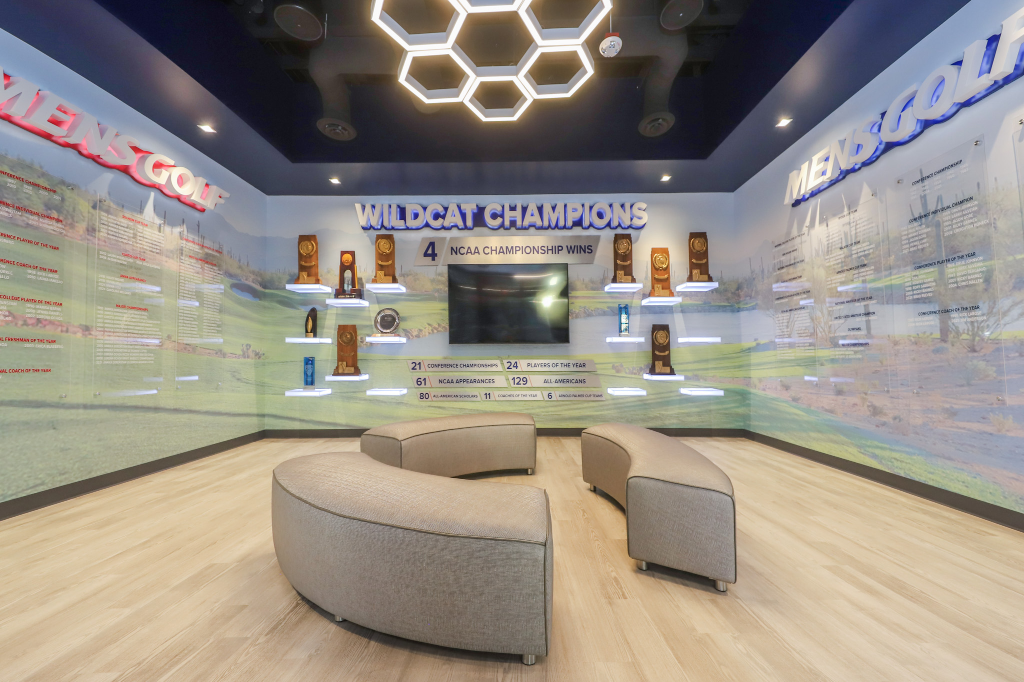 Interior of an open room with golf awards on the wall and rounded benches in the center