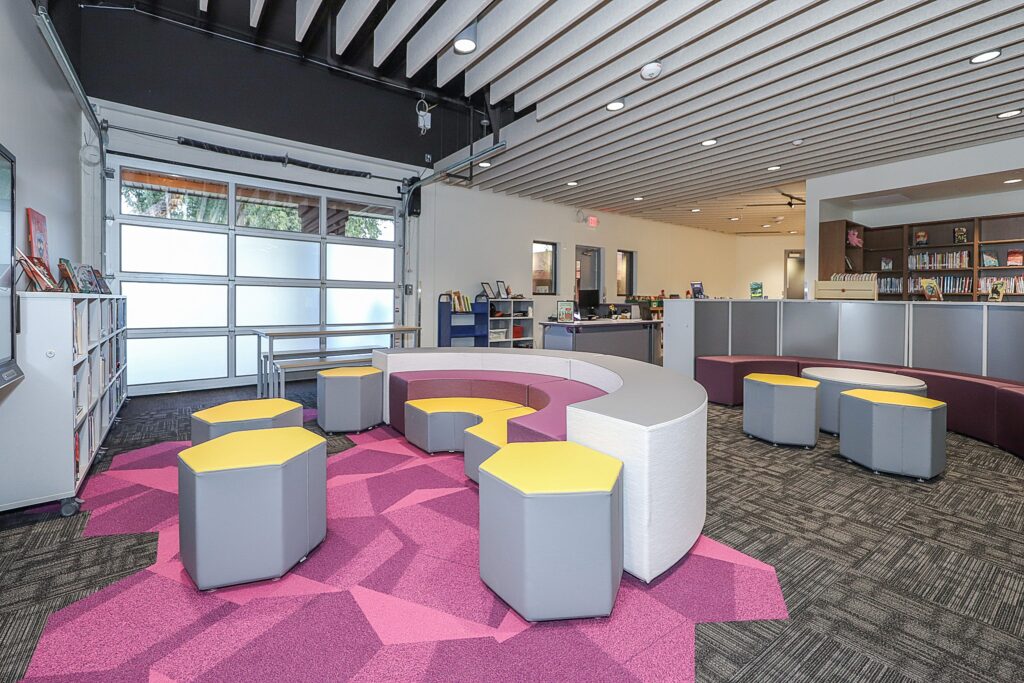 Interior of K-12 media center with yellow stools and an arch-shaped bench.