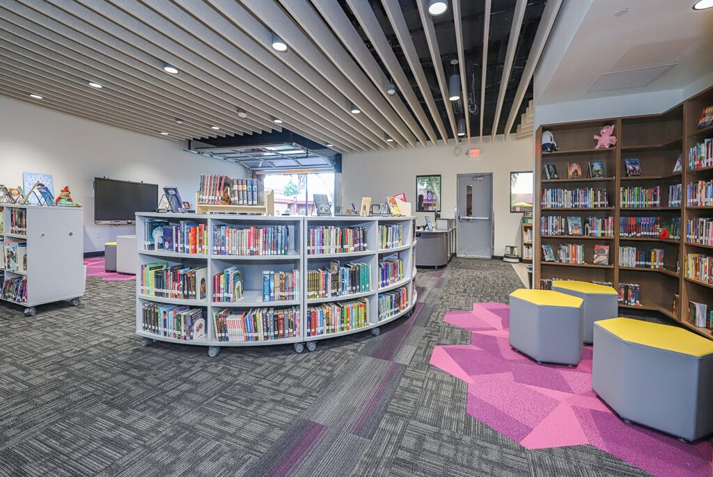 Elementary school library and media center with book-filled shelves and yellow stools.