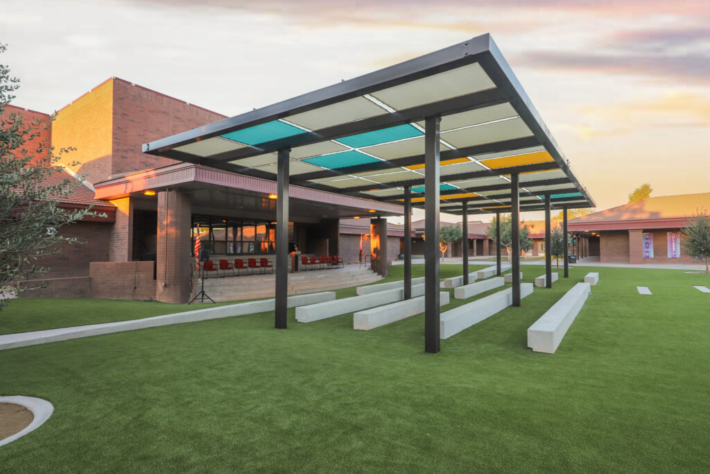 Outdoor amphitheater with concrete benches and a multicolored shade structure.