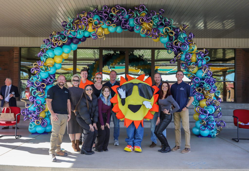 Concord staff posing with Sanborn sun maschot under balloon arch