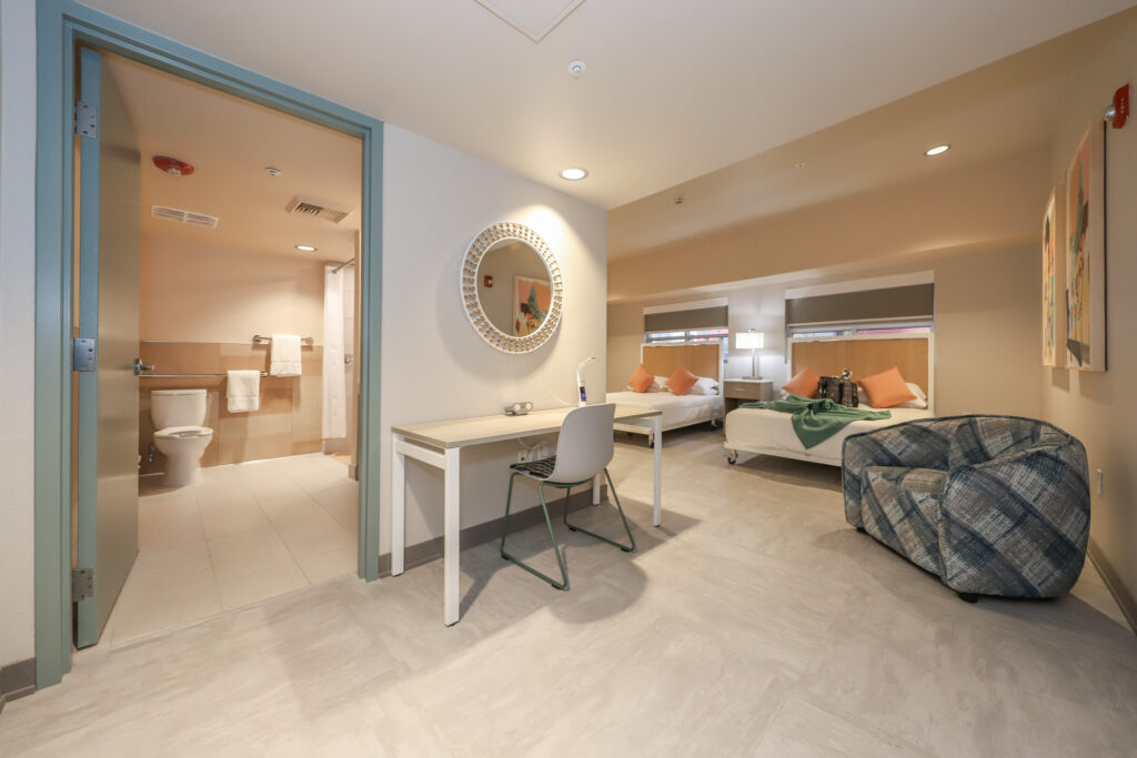 Interior of studio apartment, with two beds, loveseat, and bathroom.