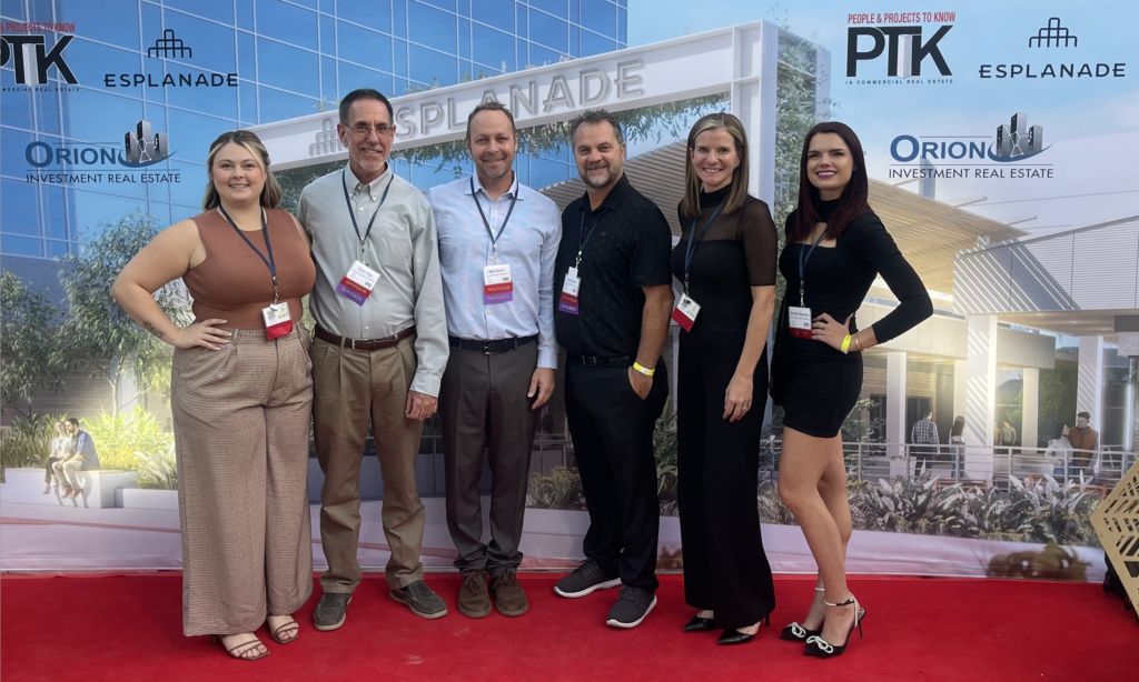 Five Employees dressed in business casual at an awards event for AZRE PTK standing in front of a step and repeat wall and on a red carpet.