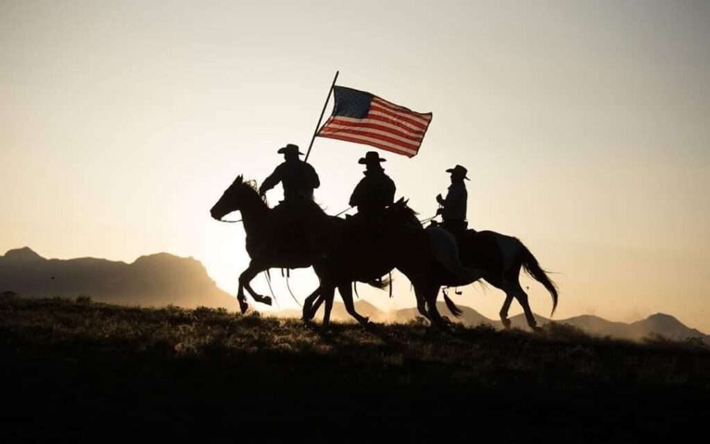 silhouette of three riders on horseback with an American flag