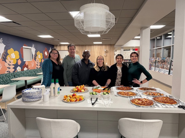 Concord Employee Owners standing behind a counter with pizza, fruit, and plates